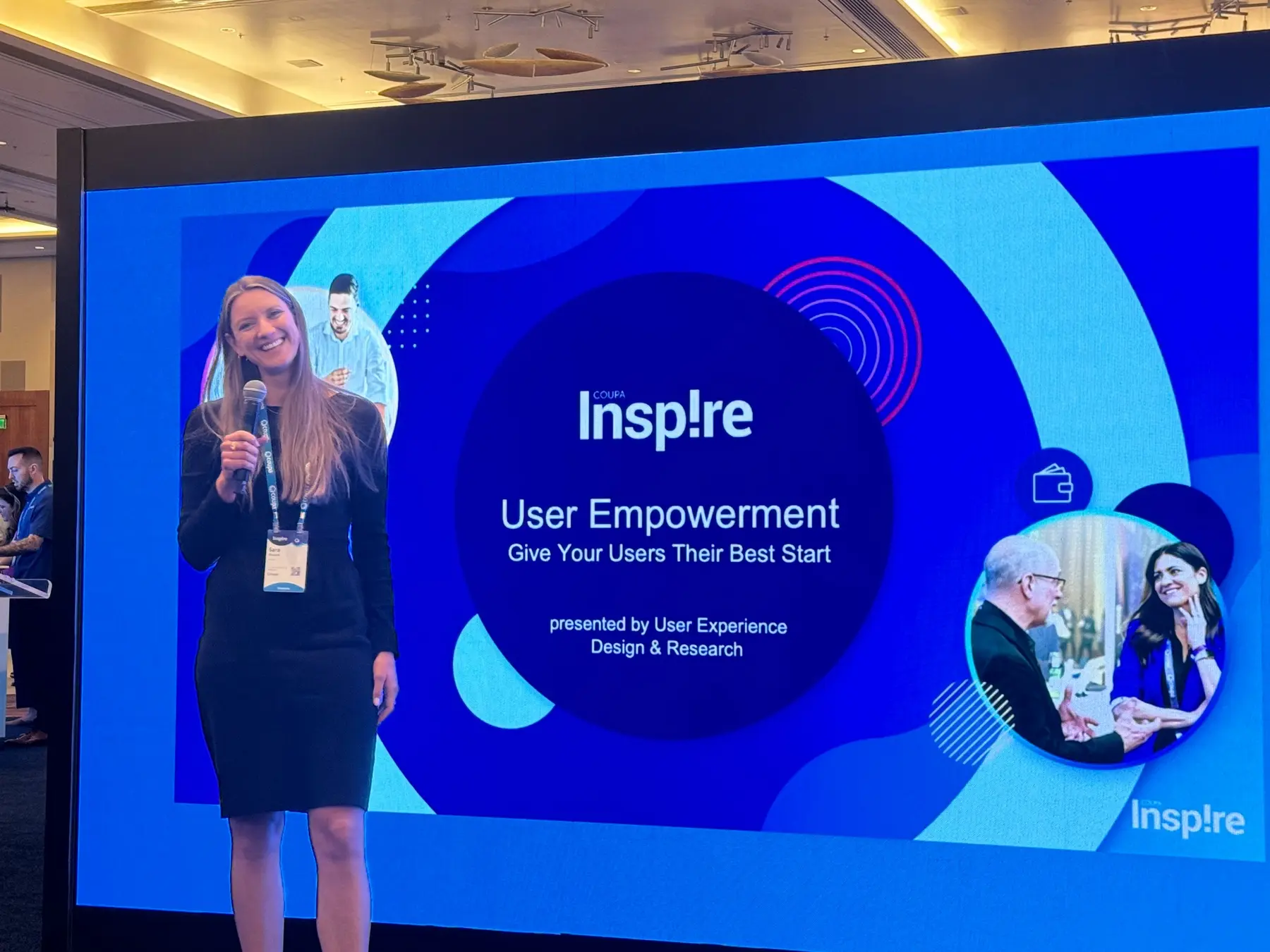 Sara smiling with a microphone beside the Coupa Inspire UX presentation screen